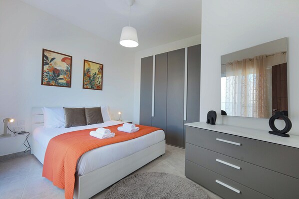 Une chambre à coucher moderne avec un lit, une armoire grise et des œuvres d’art accrochées au mur.