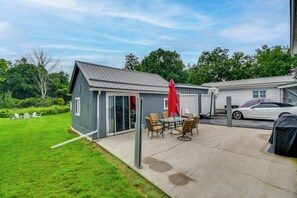 A small, single-story building with a metal roof, a covered patio area with a table and chairs, and a white car parked in the background. - Fall Retreat : 1 Mi Cayuga Lake : Gym & Fire Pit (Seneca Falls)