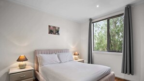 A bedroom with a bed, bedside tables, a window with curtains, and a small picture on the wall.
