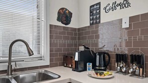 A modern kitchen with a stainless steel sink, a coffee machine, and a coffee bar sign.