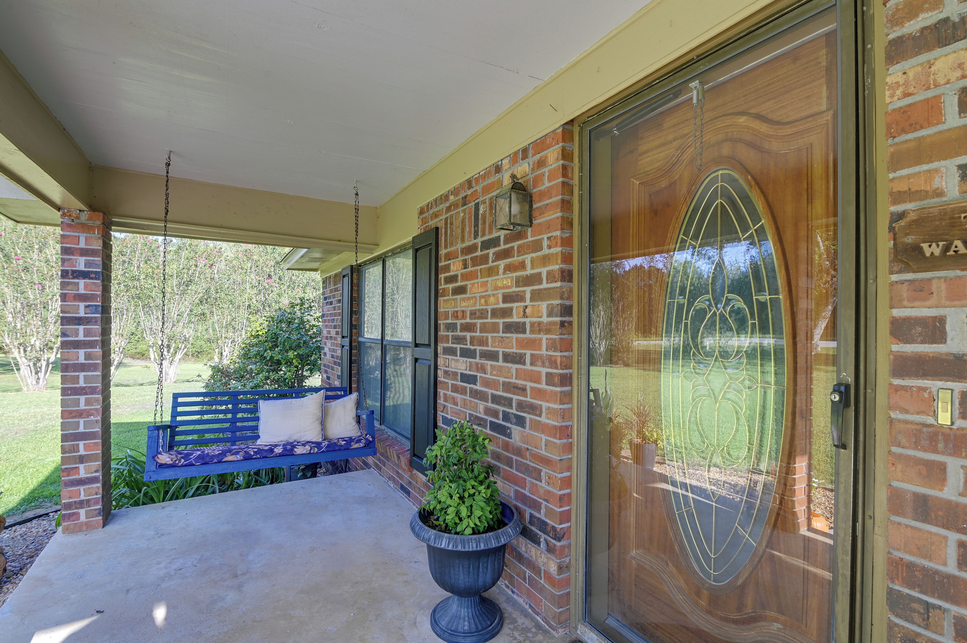 A covered porch with a bench, a potted plant, and a wooden door with a glass panel.
