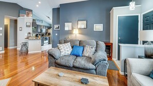 A modern living room with a grey sofa, wooden coffee table, and a kitchen in the background. - Castlerea Casa Columbus Home w/ Deck & Yard (Columbus)