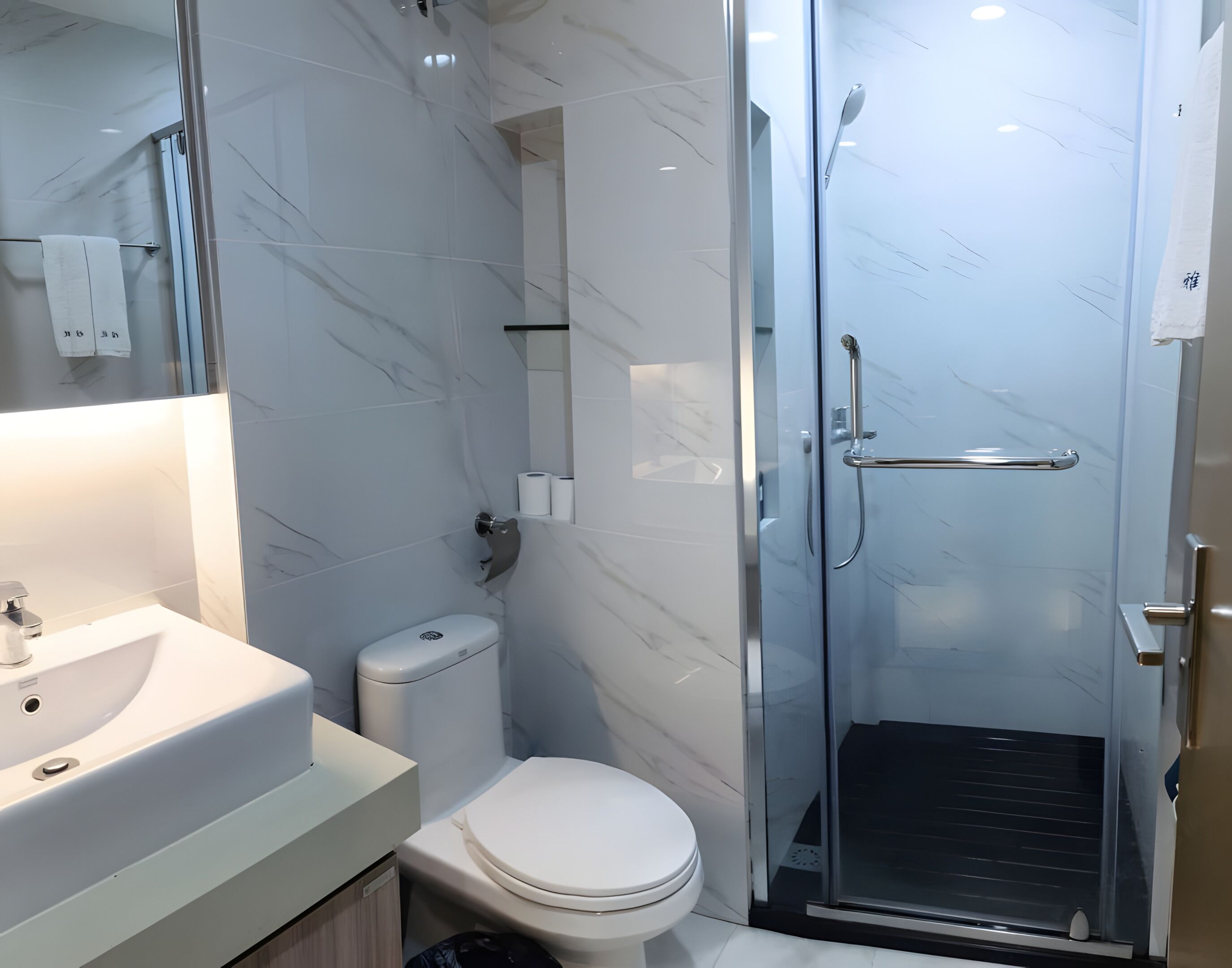 Un baño moderno con ducha envuelta en vidrio, inodoro blanco y lavamanos con espejo.