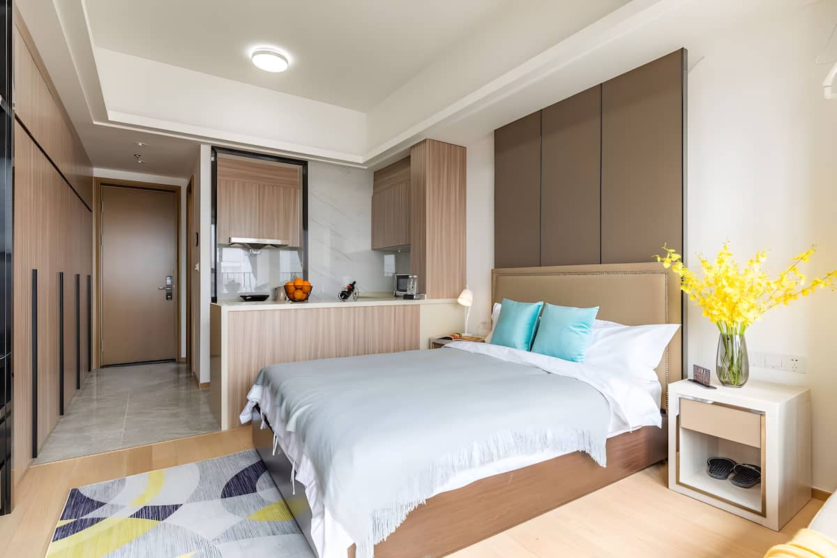 Una habitación de hotel moderna con una cama grande, una mesita de noche y una pequeña cocina.