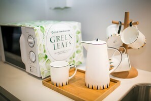 Un microondas, una caja con la etiqueta 'Good Mountain's Green Leaves' y una bandeja con tazas blancas y un hervidor de tetera.