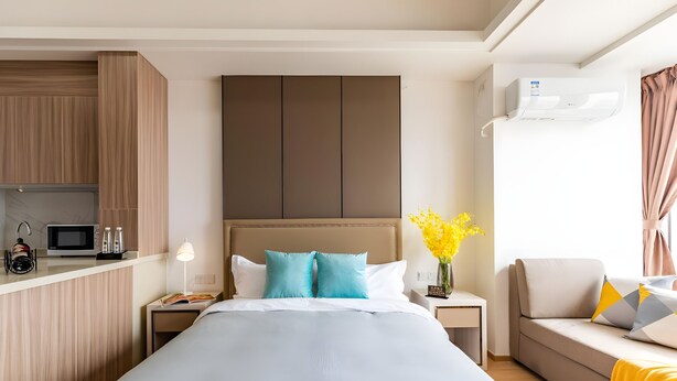 A modern hotel room with a large bed, a bedside table with a lamp, a small desk, a sofa, and a kitchen area with a microwave. - Yazhi Apartment (Guangzhou)