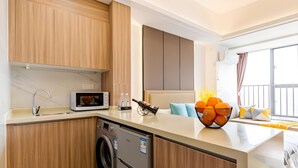 A modern kitchen with wooden cabinets, a built-in washing machine, and a microwave. - Yazhi Apartment (Guangzhou)