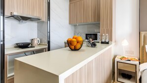 A modern kitchen with a central island, wooden cabinets, a microwave, and a small bedside table with a lamp. - Yazhi Apartment (Guangzhou)