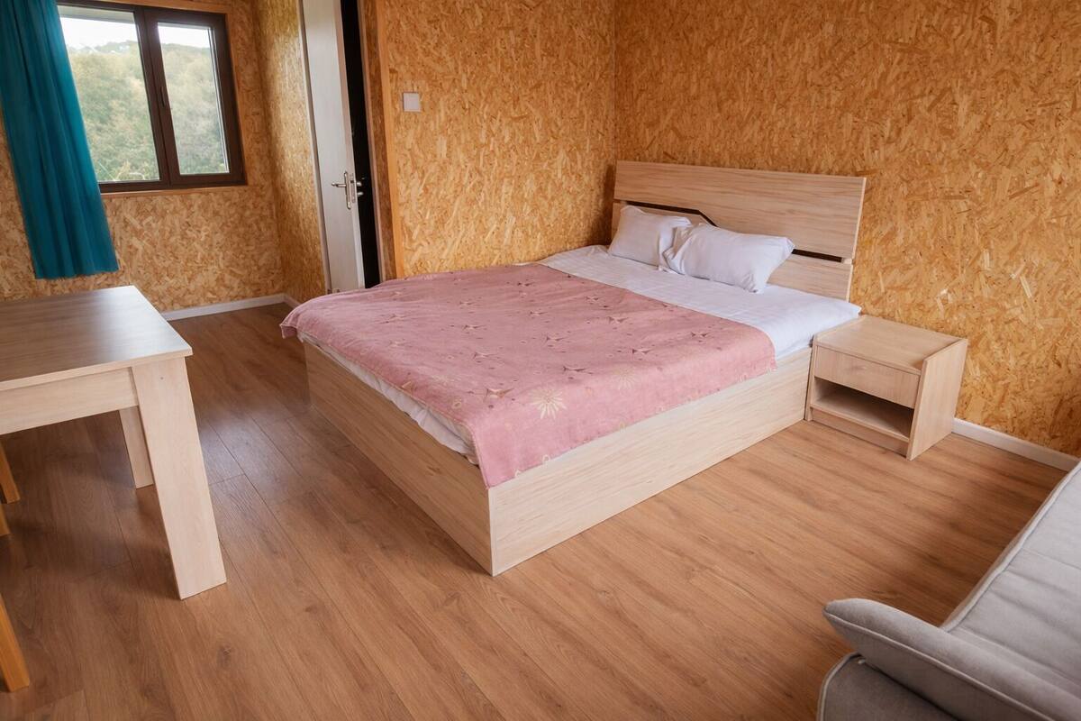 A bedroom with a wooden bed, a bedside table, a chair, and a window with curtains.