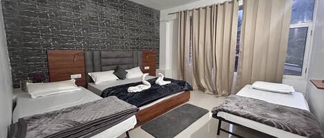 Habitación de hotel con pared de ladrillo, dos camas, ventilador de techo y ventana con cortinas.