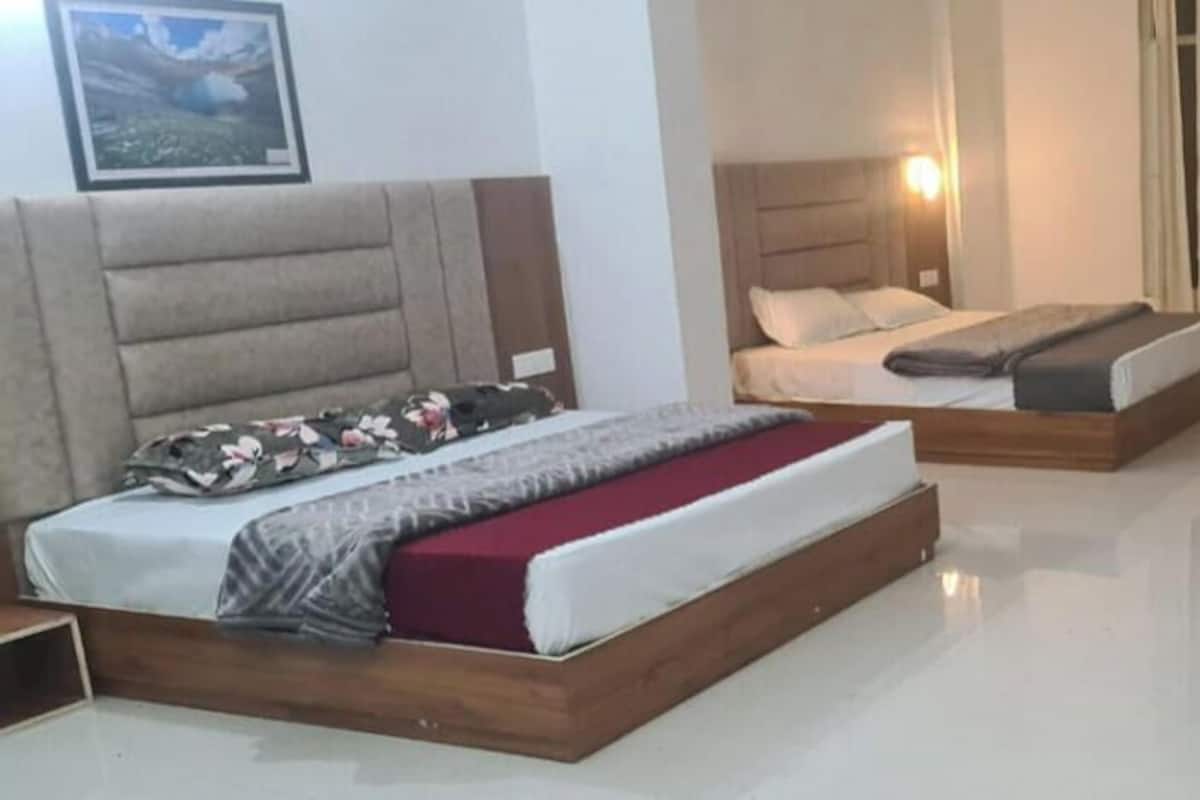 A bedroom with two beds, a wooden nightstand, and a small table with a pink mug.