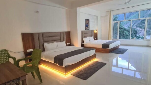 A modern hotel room with two beds, a dining table, and a view of a mountainous landscape. - Hotel Gurudeva  (Joshimath)