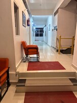 A hallway with a red mat, orange chairs, a fire extinguisher, and a staircase leading to another room.