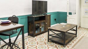 A room with a television on a stand, a cabinet with glass doors, a table with a bowl and a glass, and patterned floor tiles. - Traditional Maisonette - Yard & Jacuzzi (Mgarr)