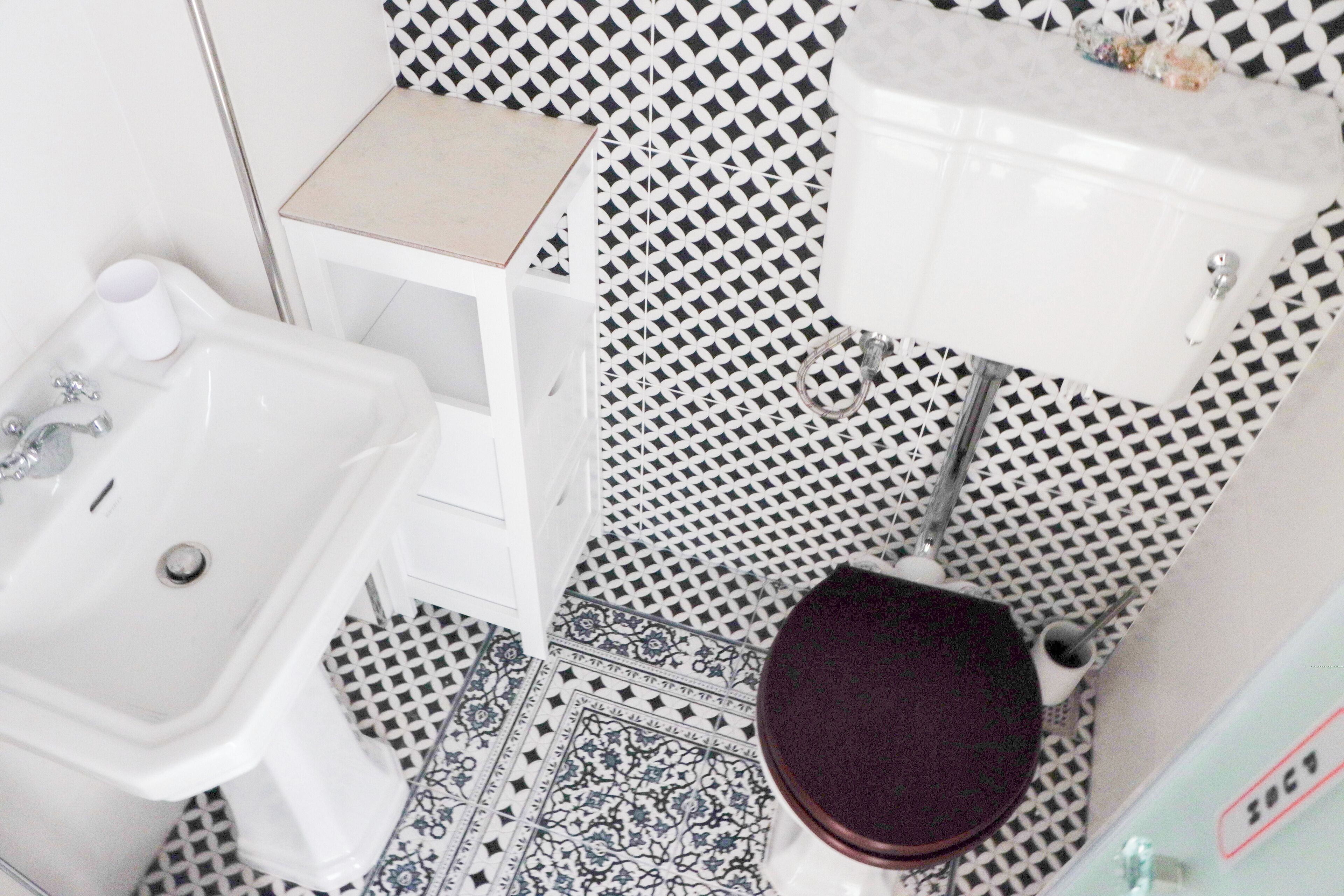 A bathroom with a toilet, bidet, and sink. The floor has a black and white patterned tile design.