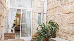A stone-walled room with a wooden bench, a potted plant, and a sliding glass door leading to a bed and a bathroom. - Traditional Maisonette - Yard & Jacuzzi (Mgarr)