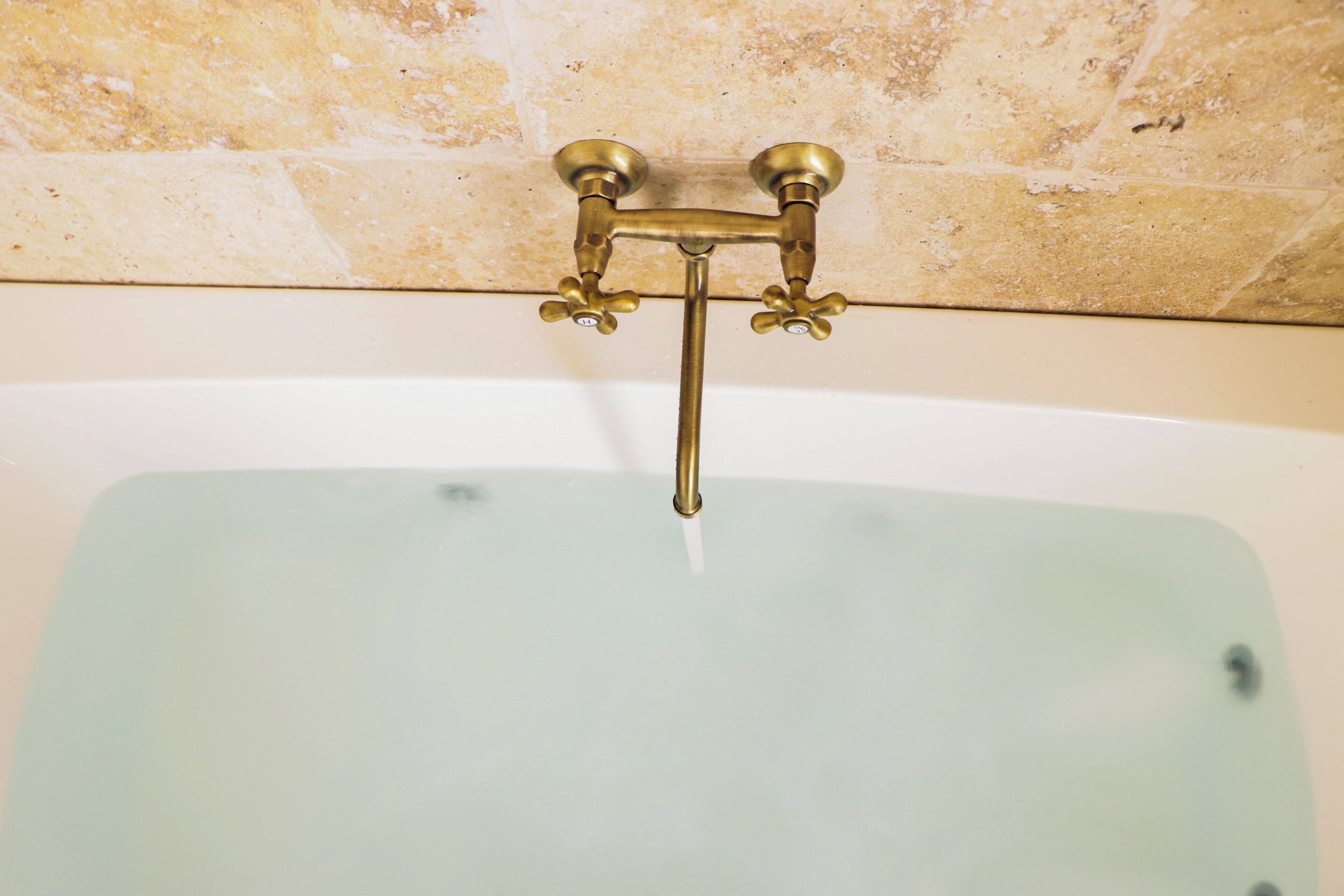 A bathtub with a glass panel and brass fixtures.