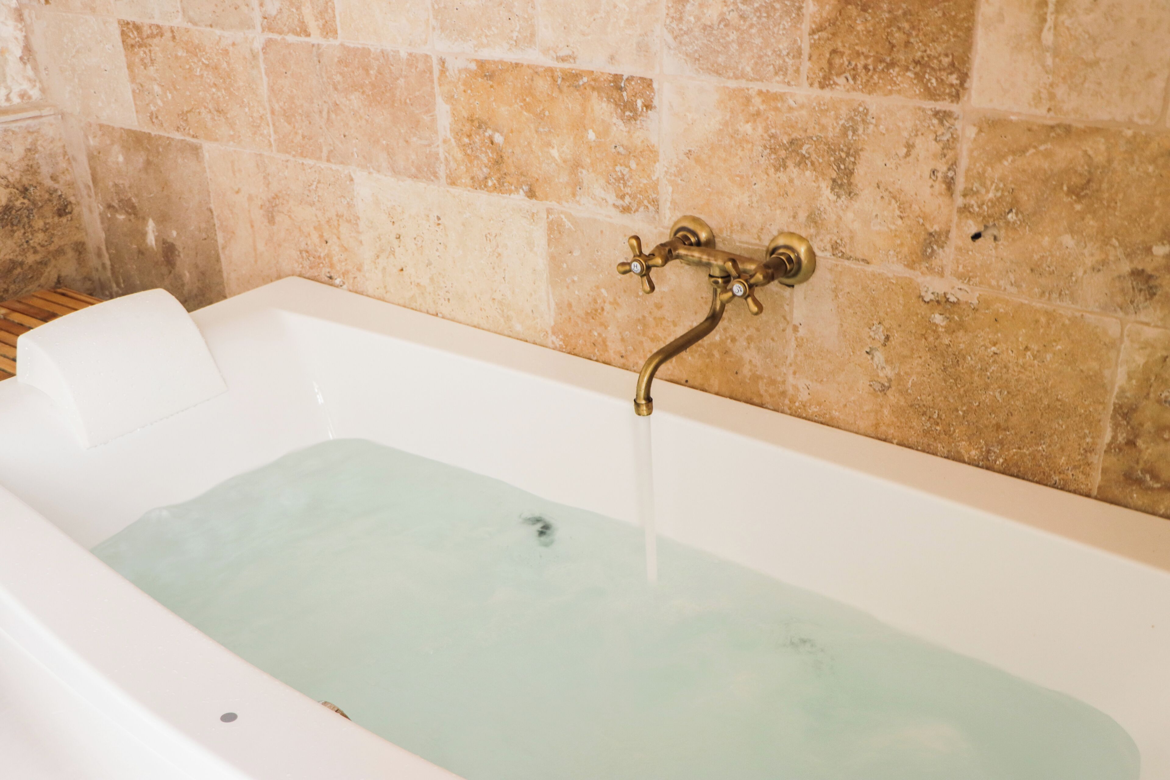 A bathtub with running water, a wooden floor, and a stone wall.