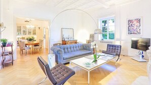 A spacious living room with a blue sofa, a coffee table, and a television. There is a dining area with a wooden table and chairs. - Villa Astarte: An elegant apartment located in the center of Sorrento, with Free WI-FI. (Sorrento)