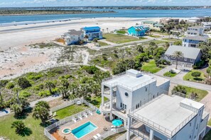An aerial view of a coastal property with a swimming pool, multiple buildings, and a beach.