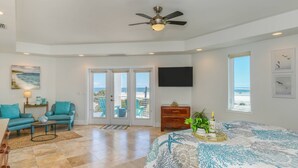 Un dormitorio con cama, ventilador de techo, televisor y vista a la playa.