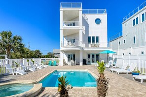 A two-story building with a swimming pool, outdoor seating, and a white fence.