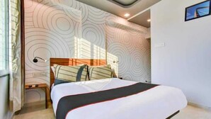 A modern hotel room with a large bed, a nightstand, and a wall with a circular pattern. - hotel manomay homes (Nagpur)