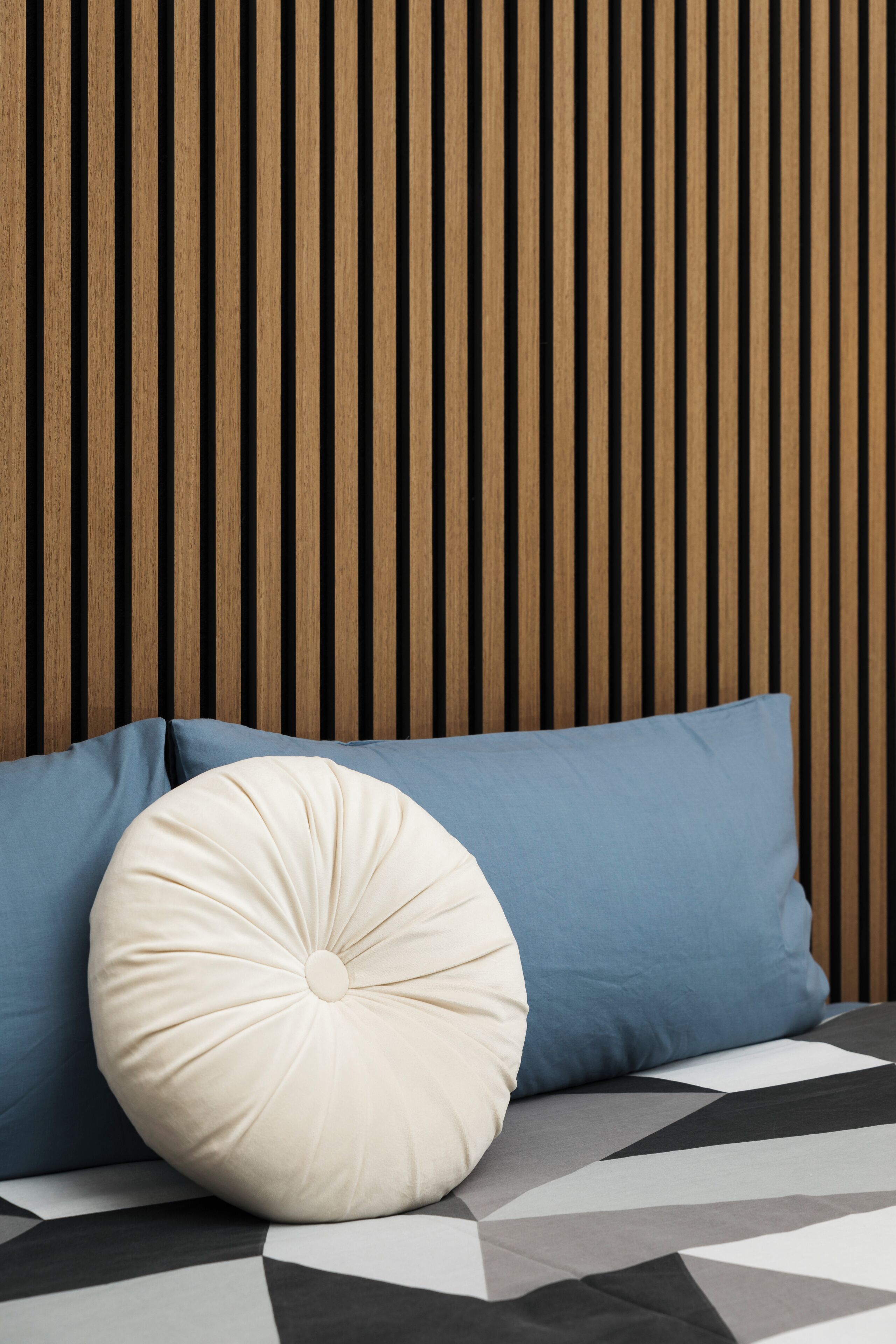 A bed with a geometric patterned bedspread, two pillows, and a wooden slat headboard.