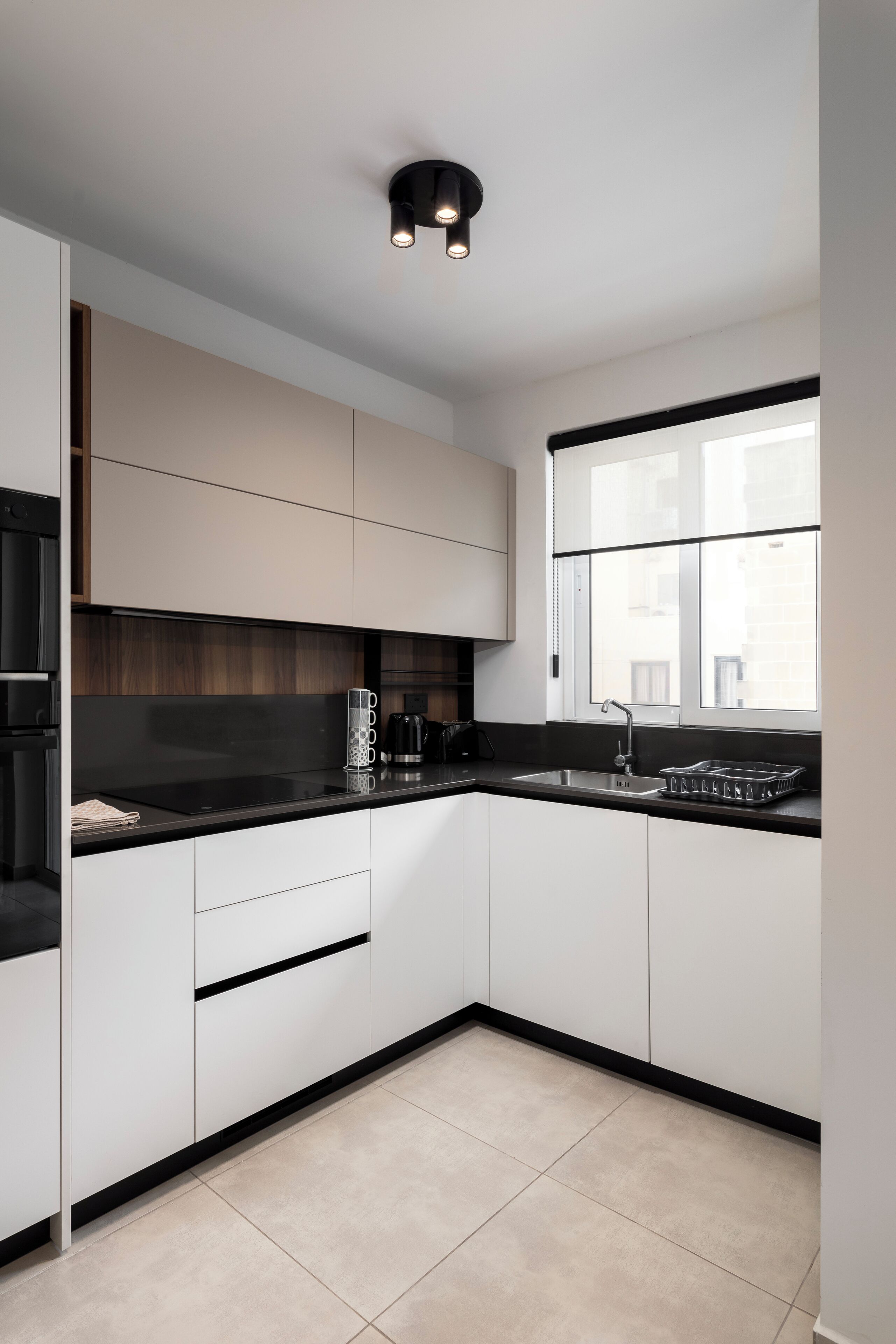 Una cucina moderna con pensili bianchi, piani di lavoro neri e una finestra che offre luce naturale.