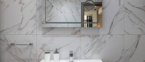 A bathroom with a marble wall, a white sink, a mirror, and a towel rack.