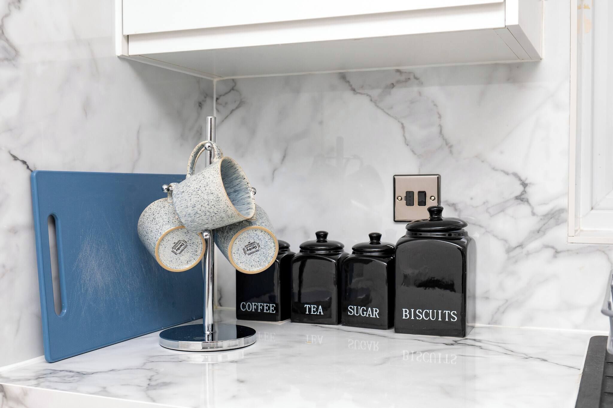 A kitchen counter with a coffee machine, tea jars, sugar containers, and biscuit jars.