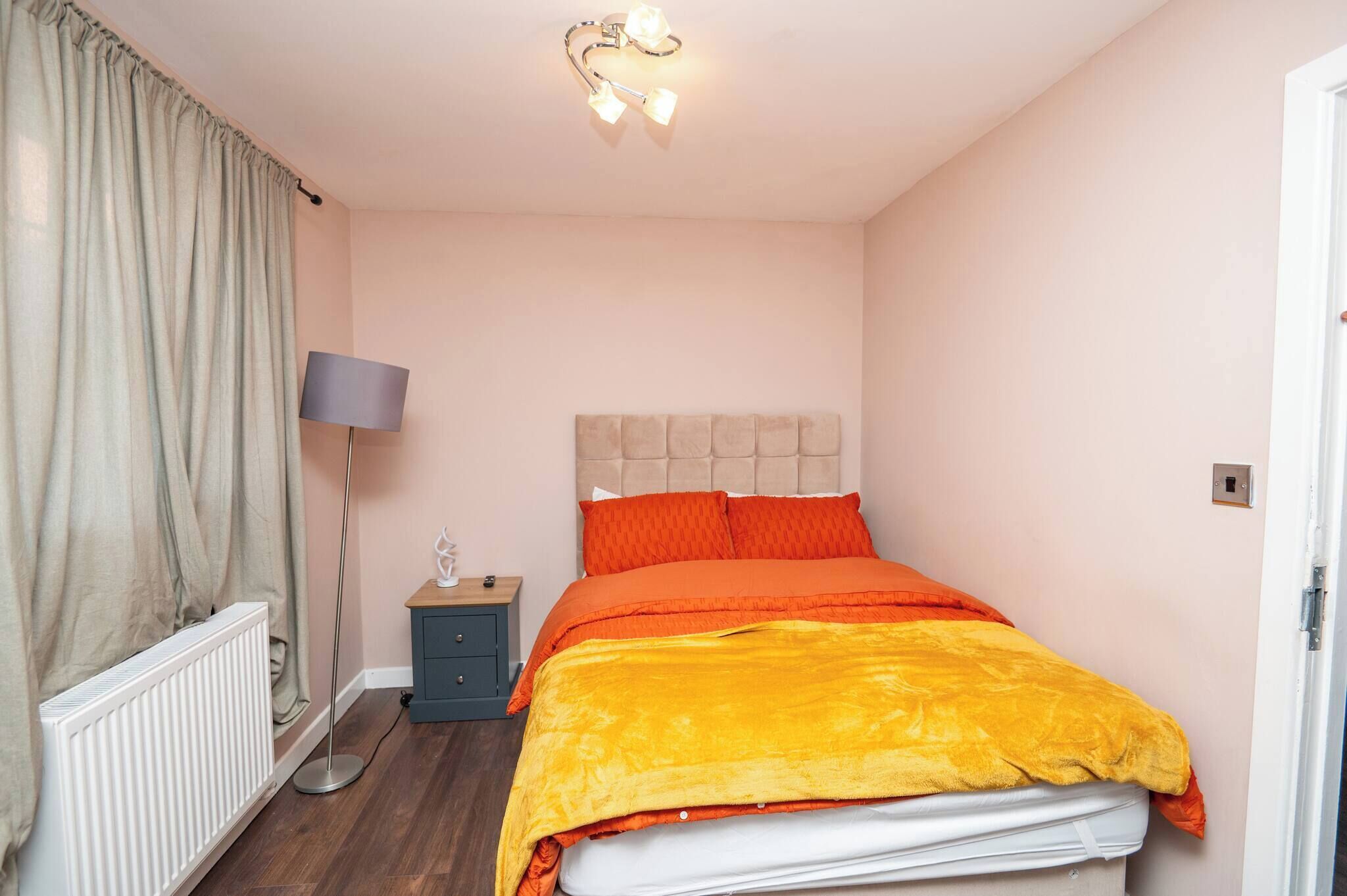 A bedroom with a bed, a bedside lamp, a nightstand, and a radiator.