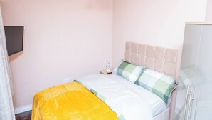 Een slaapkamer met een bed, nachtkastje, lamp en een kledingkast.