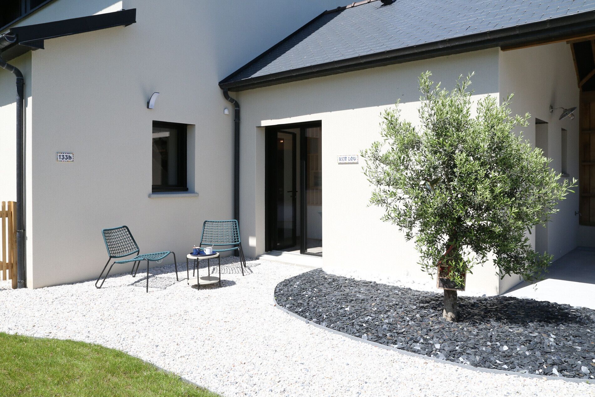 A building with a gravel patio, two chairs, a small table, and a tree.