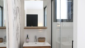 A modern bathroom with a white sink, a mirror above it, and a glass shower door. - Ker Lou (Cancale)