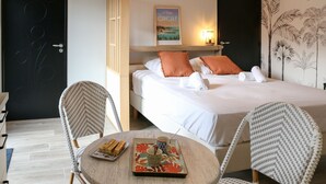 A hotel room with a bed, two chairs, a table with a tray of chocolates and a floral mug, and a poster on the wall. - Ker Lou (Cancale)