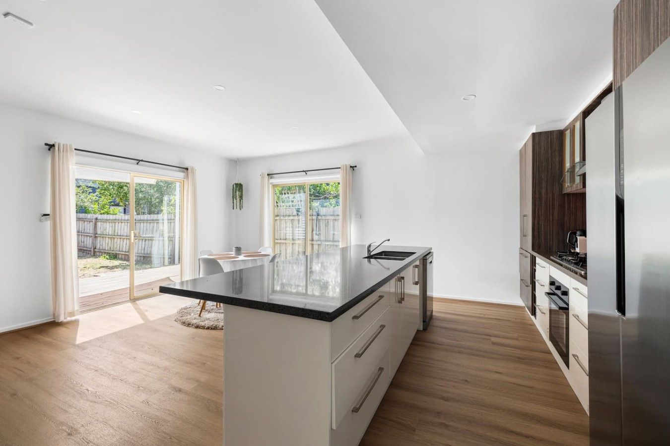 A modern kitchen with a central island, wooden flooring, and a sliding glass door leading to a backyard.