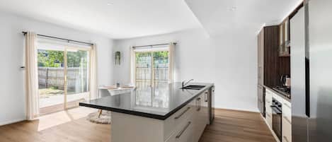 A modern kitchen with a central island, wooden flooring, and a sliding glass door leading to a backyard.