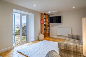 Ein Wohnzimmer mit großem Fenster, Bücherregal, Flachbildfernseher und einem karierten Sofa.