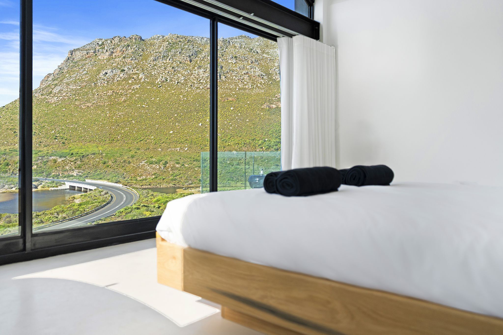 A bedroom with a large window overlooking a mountainous landscape and a road.