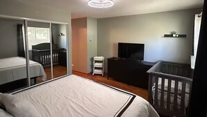 Ein Hotelzimmer mit Bett, Schreibtisch, Fernseher, Babybett und Spiegel.