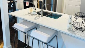Eine moderne Küche mit weißen Schränken, Edelstahlgeräten, einer Spüle und einer Bar mit Sitzgelegenheiten.