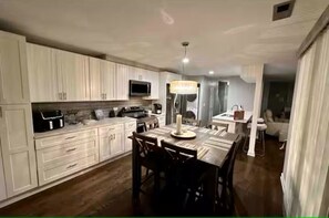 A modern kitchen with white cabinetry, a dining area with a wooden table and chairs, and a chandelier. - 3-bedroom house in delightful Aurora with cool AC and comfort (Aurora)