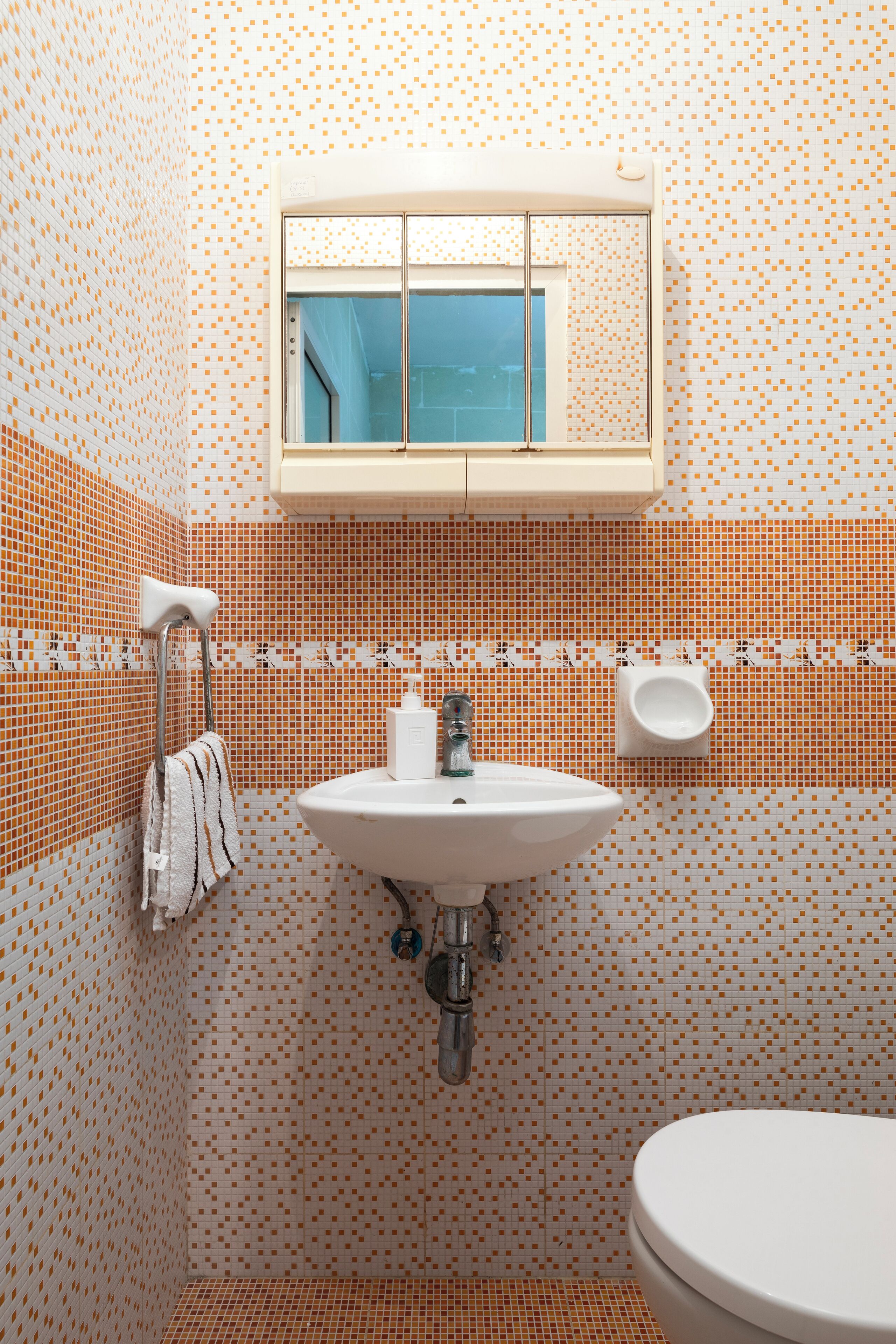 Et badeværelse med fliserede vægge, et håndvask, et spejl og et toilet.