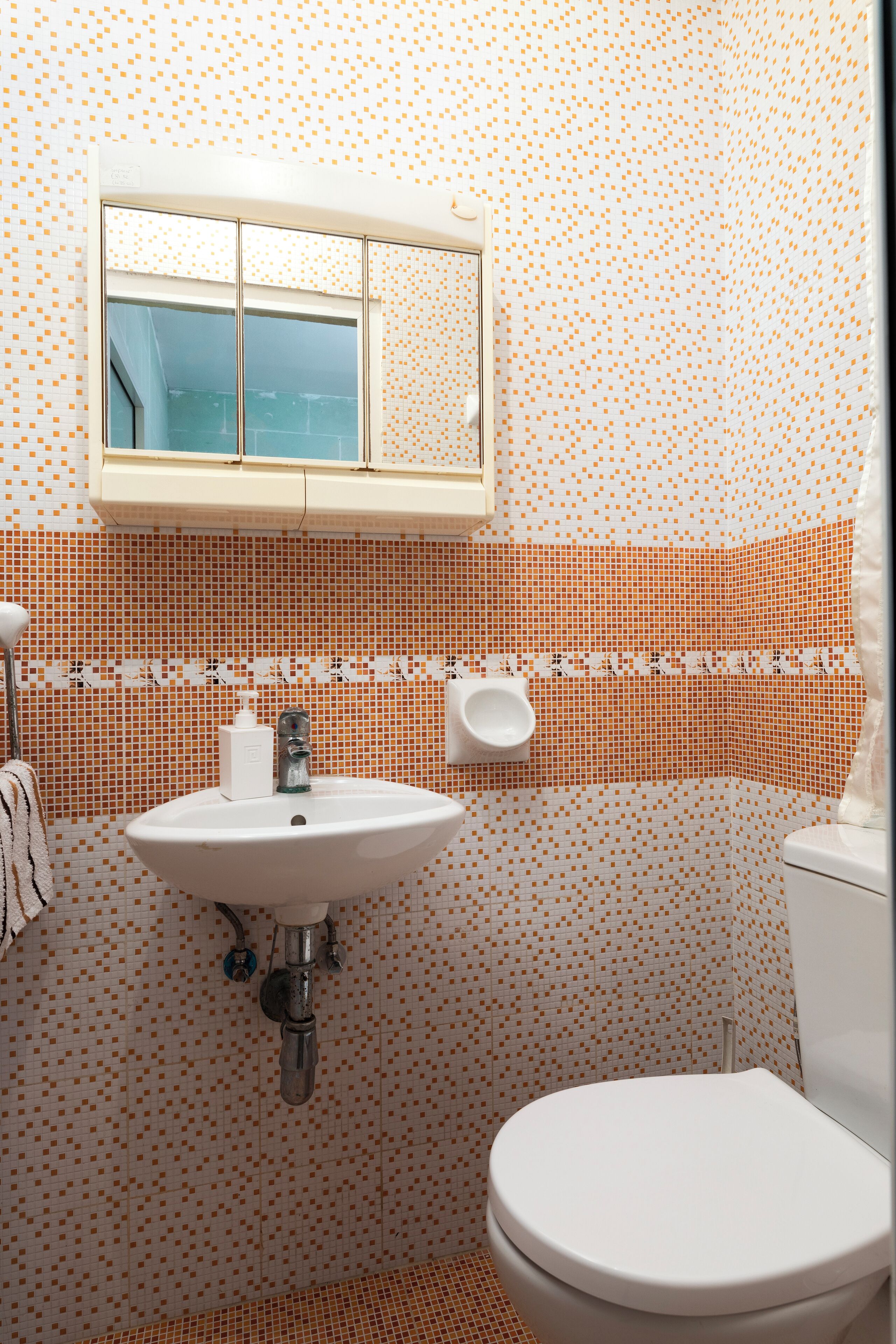 Une salle de bain avec un lavabo blanc, des toilettes et une fenêtre au-dessus du lavabo.