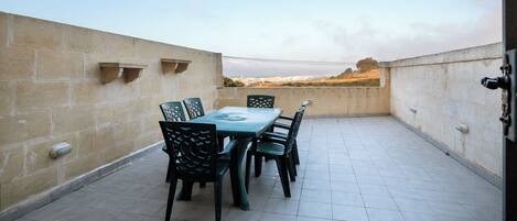 A rooftop terrace with a table and chairs, a view of the landscape, and a stone wall.