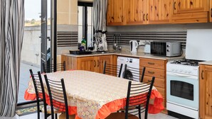 A kitchen with wooden cabinets, a dining table with chairs, a stove, a microwave, and a dishwasher. - Traditional 2BR - Terrace Country Views (Qala)