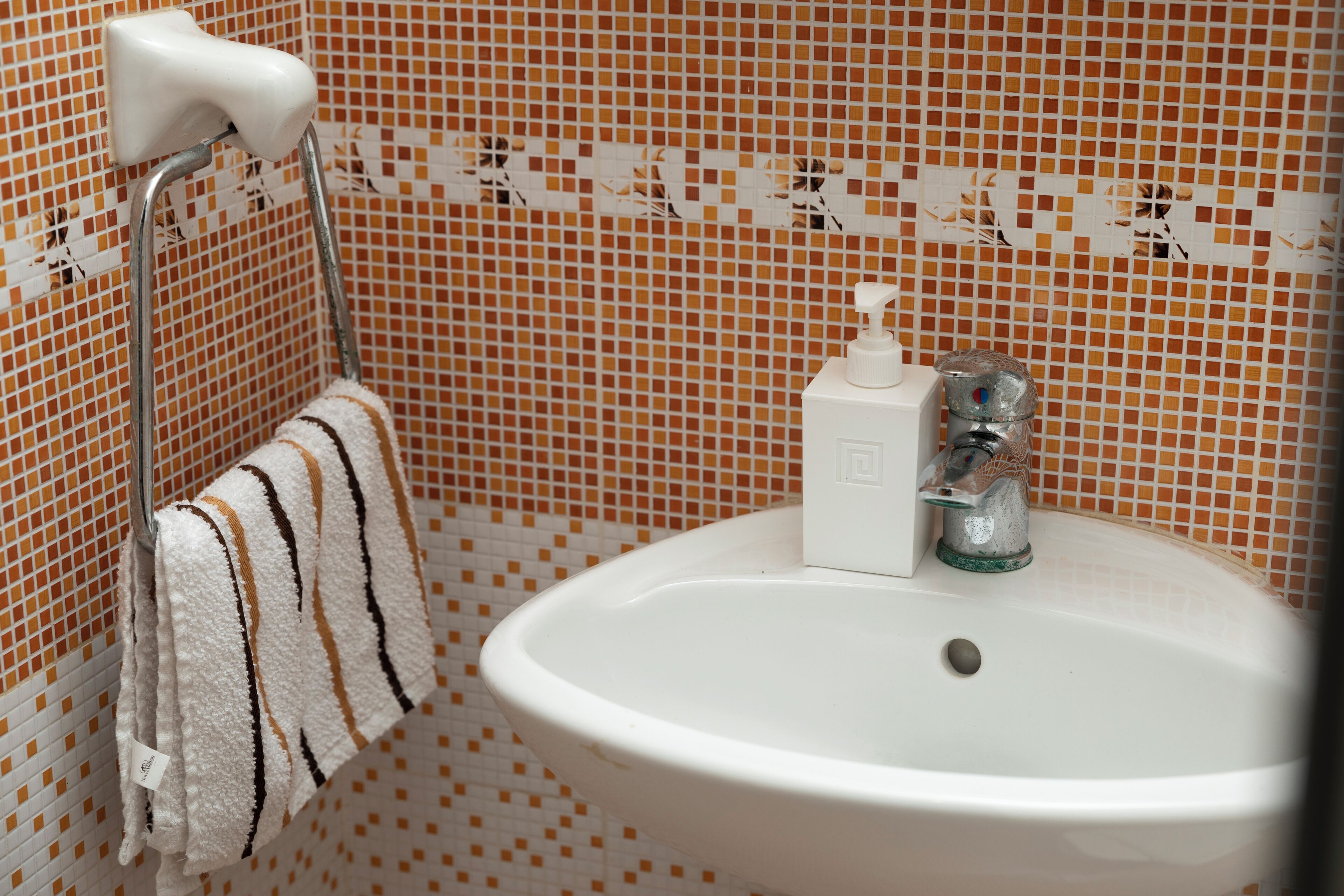 A bathroom with a white sink, a towel rack with a striped towel, and a soap dispenser.