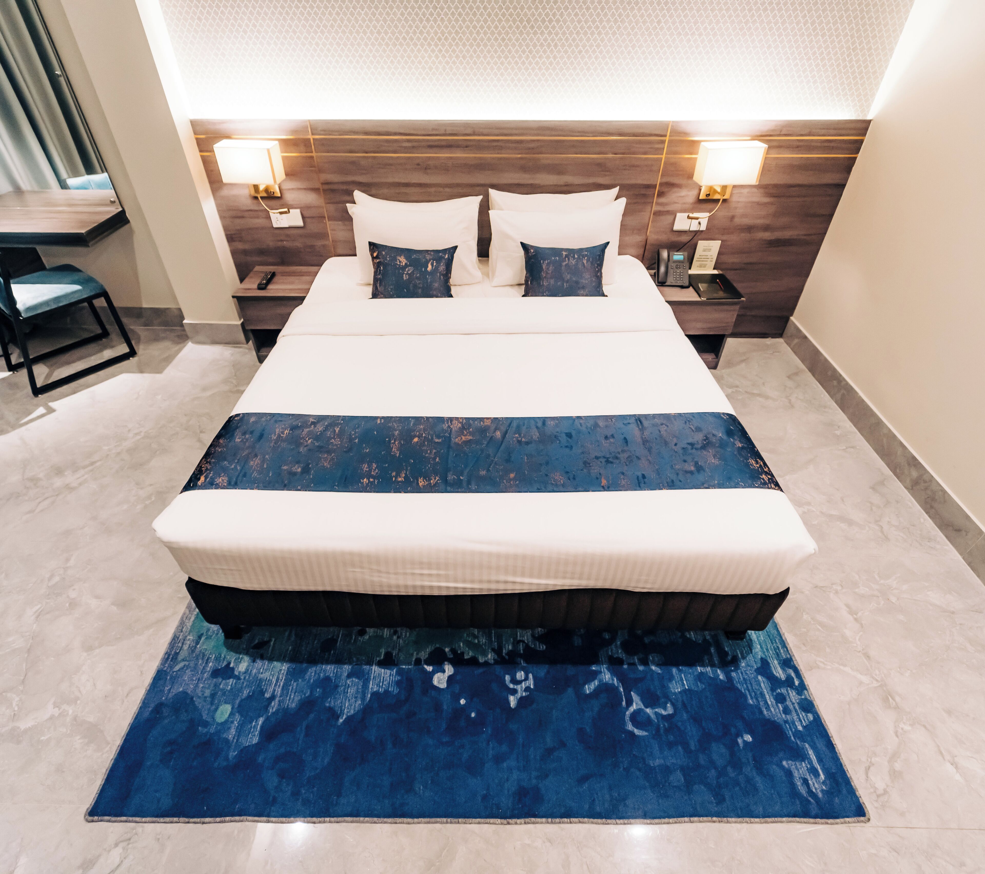 A large bed with a blue and white bedspread, two bedside lamps, and a marble floor.