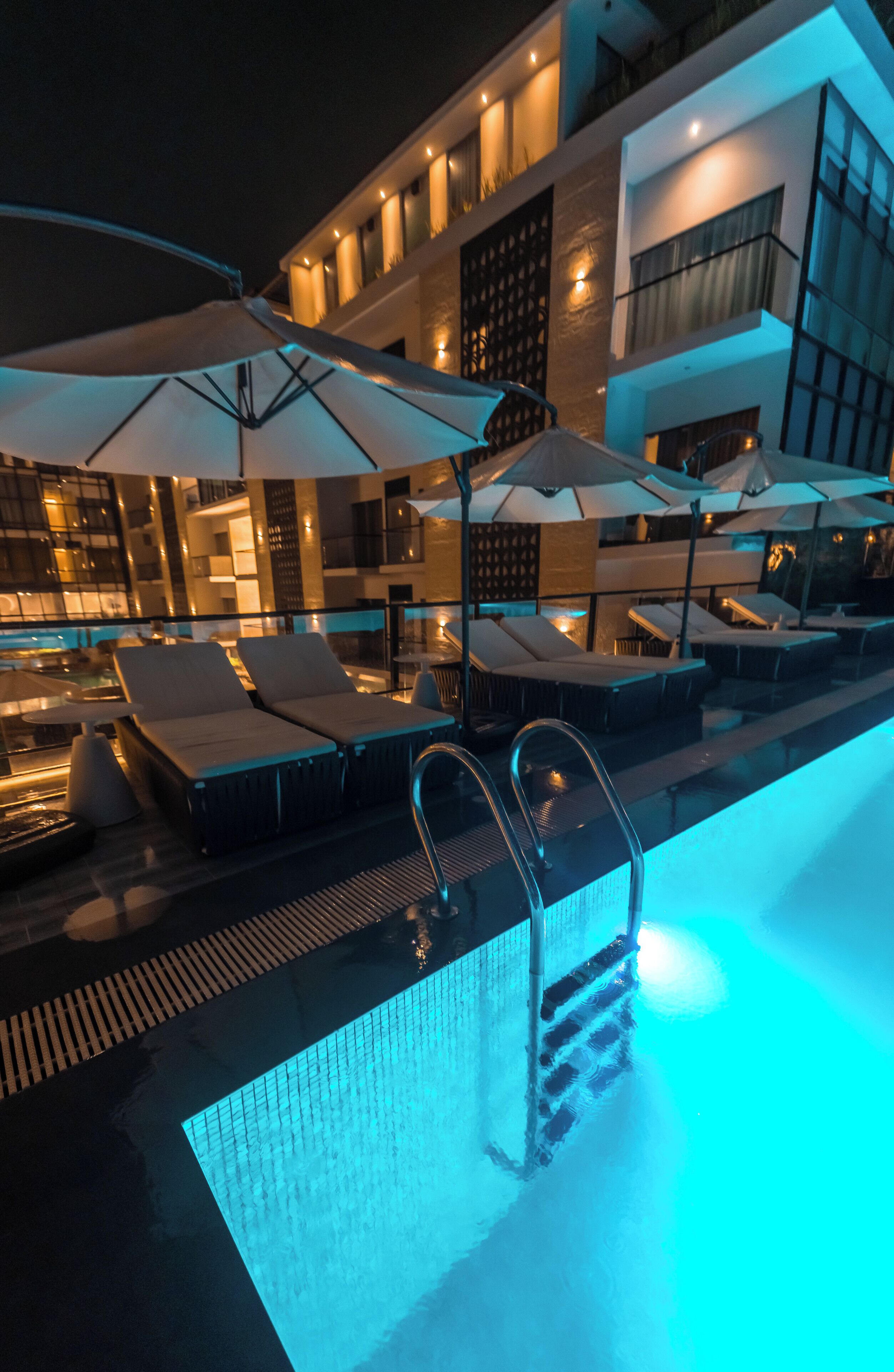 A pool area with lounge chairs and umbrellas, a poolside bar, and a building with multiple balconies.